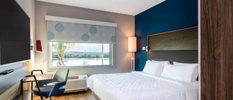A hotel room with a bed, a desk, a chair, a window with a view, and a wall-mounted TV.