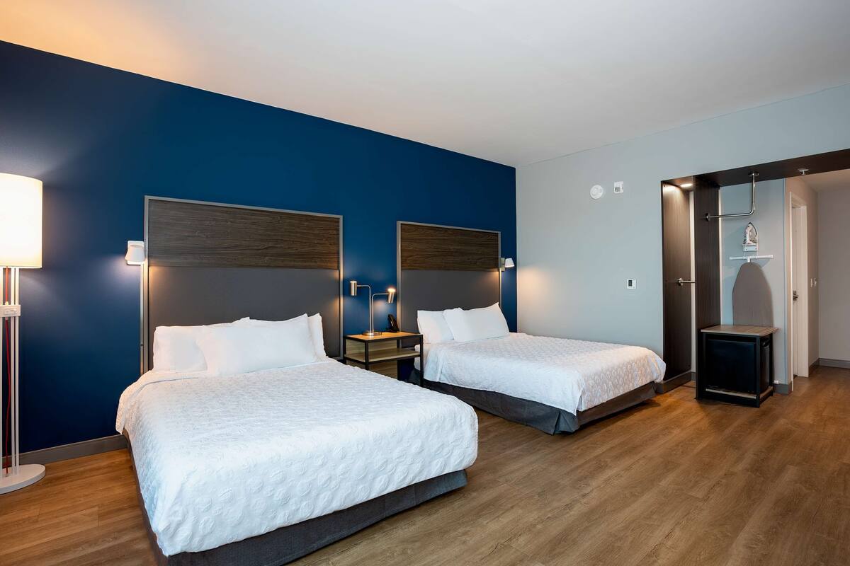 Una habitación de hotel con dos camas, una mesita de noche, una lámpara y un armario.