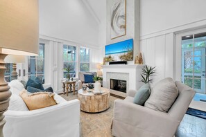 A spacious living room with a fireplace, comfortable seating, a television, and large windows.