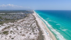 Vue aérienne d’une zone côtière comprenant une plage, une promenade en bord de mer et un quartier résidentiel.