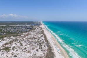 An aerial view of a coastal area with a beach, a boardwalk, and a residential area.