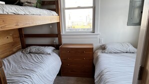A small, compact bedroom with two single beds, a wooden dresser, and a window providing natural light.