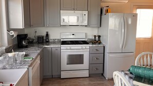 A compact kitchen with grey cabinets, a white microwave, a stove, and a refrigerator.