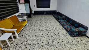 Una sala de estar con un sofá, una silla, una mesita, un adorno en la pared y una ventana con persianas.