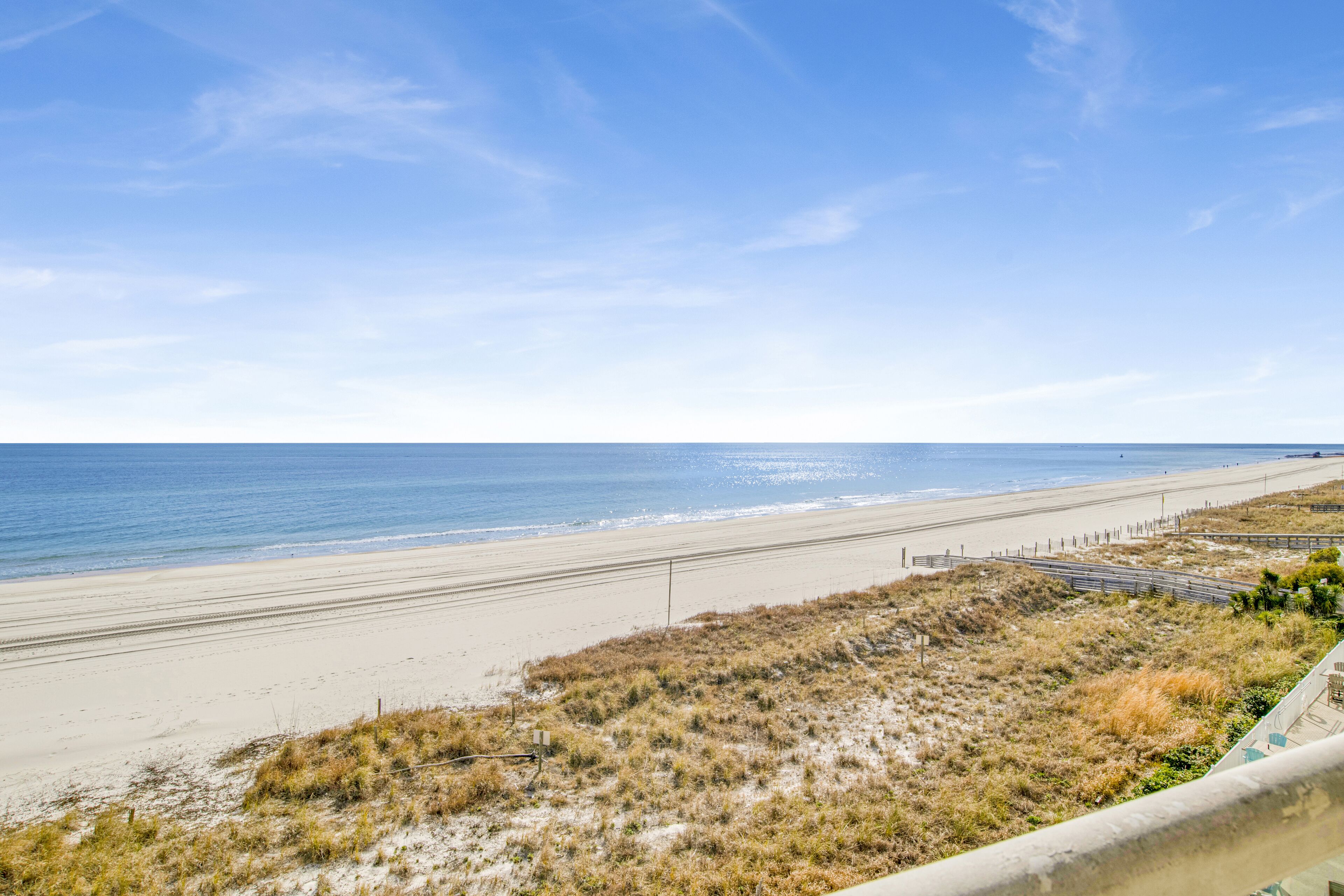 A beach with a clear sky, sandy shore, and a fence running parallel to the beach.
