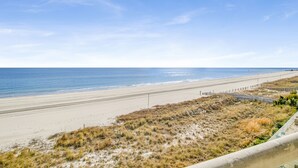 A beach with a clear sky, sandy shore, and a fence running parallel to the beach.
