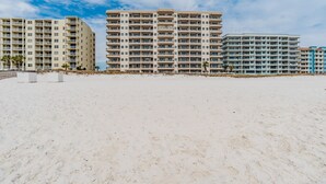 A beachfront hotel with multiple floors, balconies, and a sandy beach in the foreground.