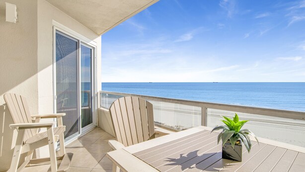 A balcony with a table and chairs, a potted plant, and a view of the ocean.