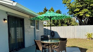 Um pátio com mesa e cadeiras, um guarda-sol verde e uma churrasqueira.