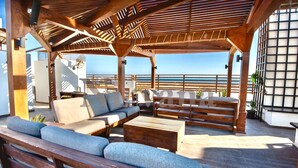 Un área de estar al aire libre con techo, muebles de madera y vista al océano.
