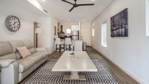 A modern living room with a beige sofa, a coffee table, and a dining area with a kitchen in the background.