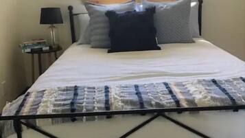 Una cama con estructura metálica, una ventana con persianas, y dos cuadros en la pared.