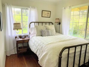 Une chambre à coucher avec un lit en métal, une table de chevet avec une lampe et une fenêtre avec des rideaux.