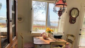 A kitchen with a checkered floor, wooden cabinets, a window with a view, a clock, and a table with chairs. - Shore Acres Ocean View Cabin and Retreat Space (McKinleyville)