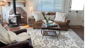 A cozy living room with a fireplace, a sofa, a coffee table, and a door. - Shore Acres Ocean View Cabin and Retreat Space (McKinleyville)