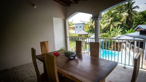 Ein Holztisch mit Stühlen auf einem Balkon mit Blick auf einen Swimmingpool und Palmen.
