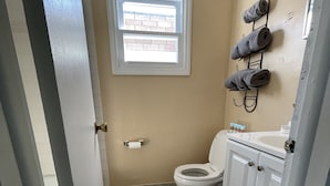 A bathroom with a toilet, a window, a towel rack, and a sink.