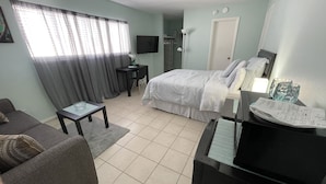 A neatly arranged bedroom with a bed, bedside table, and a desk with a chair.
