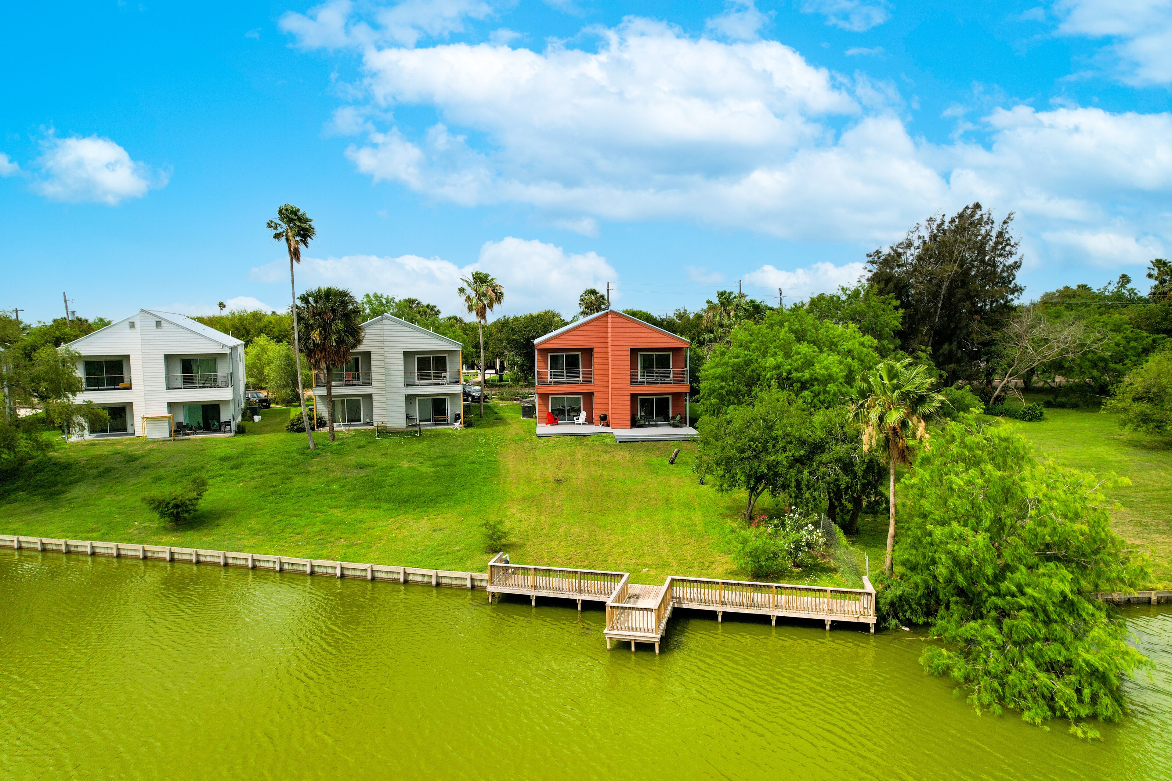 A residential area with three houses, a wooden dock, and a body of water.