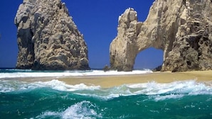 A coastal landscape with large rock formations and a sandy beach. - Father’s Day at ME Cabo Oceanfront on Medano Beach June 18-25th 2022 (Cabo San Lucas)