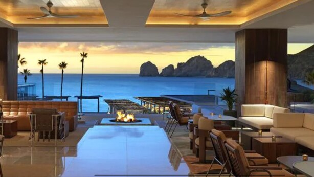 A spacious lounge area with a large fire pit, comfortable seating, and a view of the ocean at sunset. - Father’s Day at ME Cabo Oceanfront on Medano Beach June 18-25th 2022 (Cabo San Lucas)