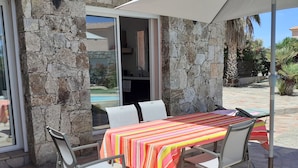 A patio with a table covered by a striped tablecloth, stone walls, and a view of a pool.