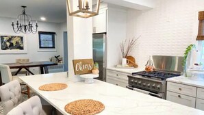 A modern kitchen with a marble countertop, a gas stove, and a dining area with a white table and chairs. - Gorgeous, Fully Remodeled Open Floor-Plan! (Pontiac)