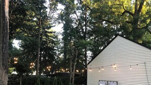 A cozy backyard with a white shed, a fire pit, a cushioned seating area, and string lights. - Gorgeous, Fully Remodeled Open Floor-Plan! (Pontiac)