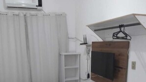 Et soveværelse med en seng, et fjernsyn monteret på en træpanel, et lille bord og en hvid klimaanlæg på væggen.