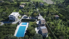 An aerial view of a residential area with a swimming pool, multiple houses, and surrounding greenery.