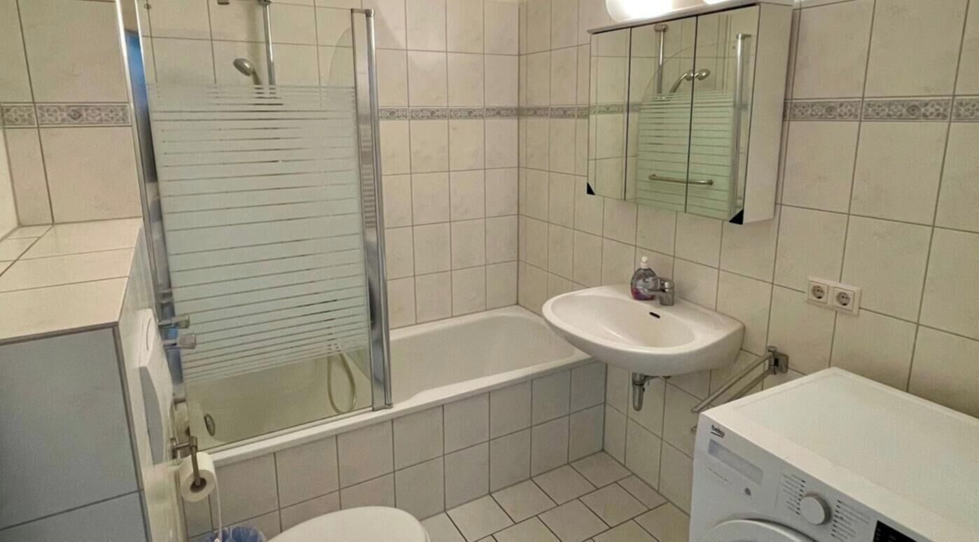 Ein Badezimmer mit Duschkabine aus Glas, Waschbecken, Spiegel und Waschmaschine.