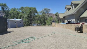 A backyard with a gravel surface, a green hose, a small shed, and a house with a sloped roof and windows. - RV spot on the River Unit C -minutes from Gorge concerts (Quincy)