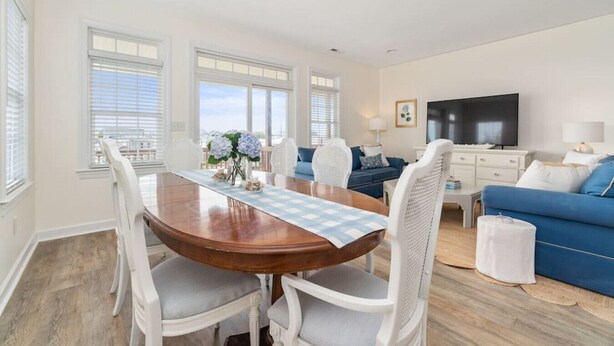 Una sala de estar moderna con una mesa de comedor de madera, sillas blancas, un sofá azul y un televisor de pantalla plana.