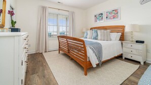 Un dormitorio con cama de madera, una mesita de noche, un aparador, un ventanal con cortinas y una pared decorada con dos cuadros.