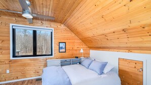 Une chambre à coucher avec un lit, des tables de chevet, un ventilateur de plafond, une fenêtre et un tableau encadré au mur.