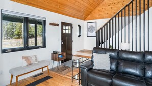 Un salon moderne avec un canapé en cuir, un banc et un escalier doté de rampes noires.