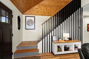 A staircase with wooden steps and black and white striped railings, leading to a landing with a white console table and a framed picture.