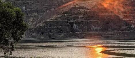 A sunset over a river with a rocky landscape in the background.