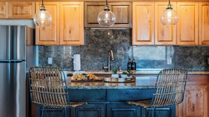 A kitchen with wooden cabinets, a stainless steel refrigerator, a marble countertop, and two wicker chairs. - Desert Oasis • Hot Tub, Pool, Arcade & Hammocks • Fenced 2 Acres • Joshua Trees (Yucca Valley)