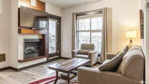 A modern living room with a fireplace, a sofa, a chair, and a coffee table. - Cozy 2 Bedroom Condo in Silver Creek Lodge (Canmore)