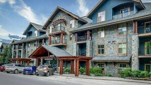 A multi-story hotel with stone facade, balconies, and a covered entrance. - Cozy 2 Bedroom Condo in Silver Creek Lodge (Canmore)