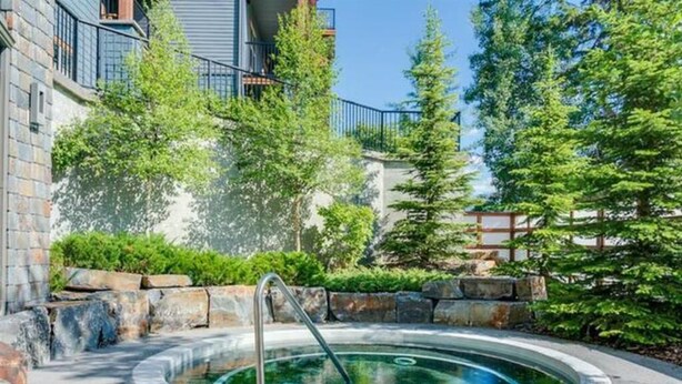 A hot tub surrounded by stone steps and greenery, with a building in the background. - Cozy 2 Bedroom Condo in Silver Creek Lodge (Canmore)