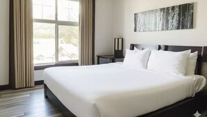 A hotel room with a large bed, a window with curtains, a bedside table, and a wall-mounted artwork. - Cozy 2 Bedroom Condo in Silver Creek Lodge (Canmore)