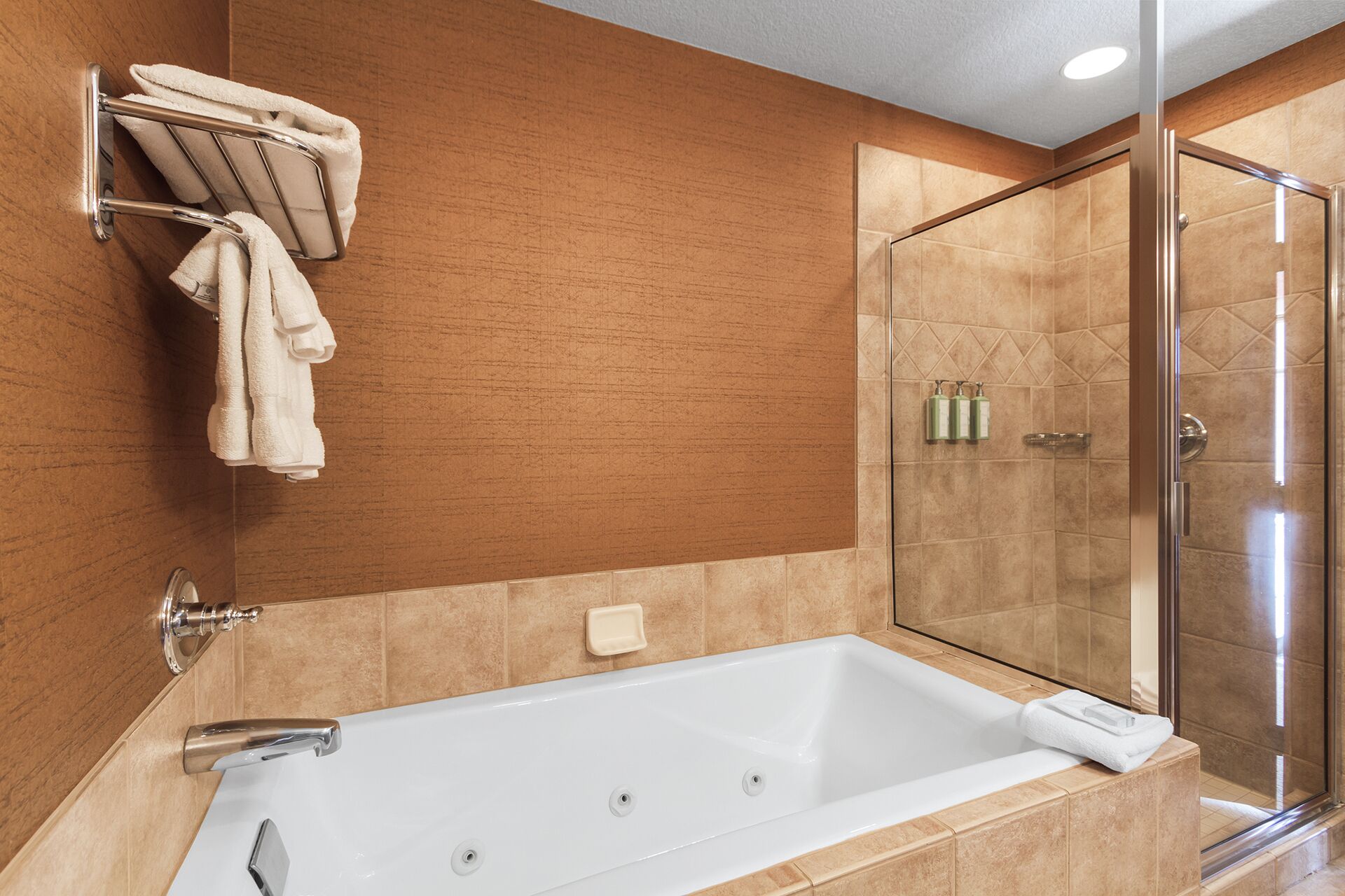 A modern bathroom with a large bathtub, a glass shower enclosure, and a towel rack with multiple towels.