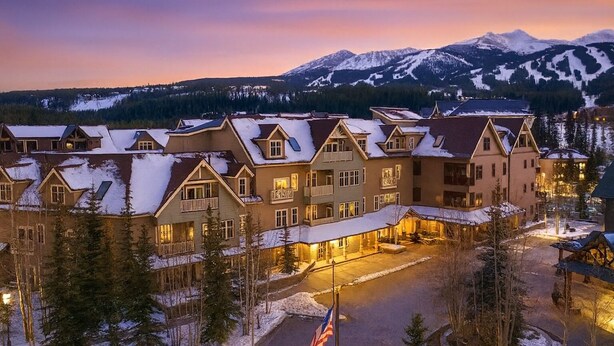A large, multi-story hotel with a symmetrical facade, snow-covered roofs, and a mountain backdrop.