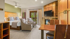 A hotel room with a bed, two armchairs, a wooden table, a TV, and a fireplace.