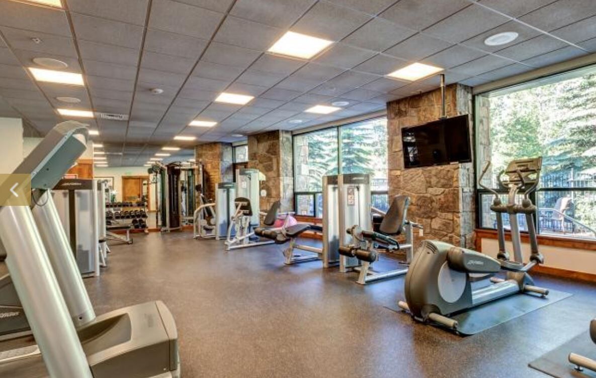 A gym with various exercise equipment, large windows, and a stone wall.