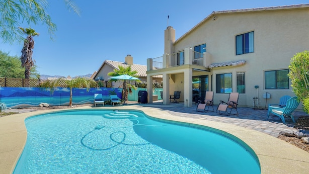 A swimming pool with clear water, surrounded by a patio area with lounge chairs and umbrellas. - Hike, Bike, Explore! Mtn-View Tucson Home (Tucson)