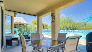 An outdoor patio with a glass table and chairs, a view of a swimming pool, and a covered area with a grill. - Hike, Bike, Explore! Mtn-View Tucson Home (Tucson)