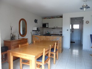Uma cozinha compacta com micro-ondas, torradeira e armários de madeira. Há uma mesa de jantar com cadeiras e um espelho grande na parede.